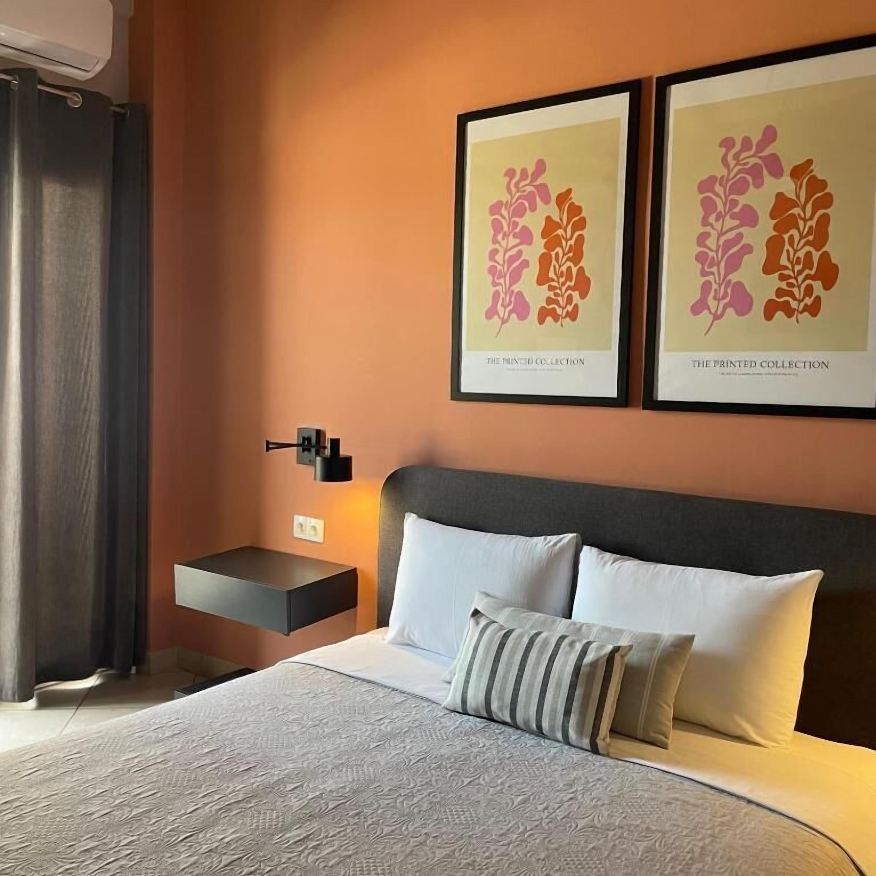 Een hotelkamer met een bed, nachtkastje, wandlamp en twee ingelijste kunstwerken aan de muur.