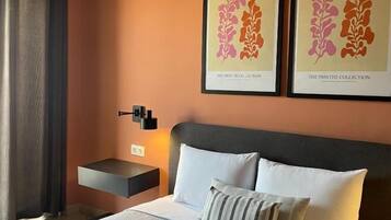Een hotelkamer met een bed, nachtkastje, wandlamp en twee ingelijste kunstwerken aan de muur.