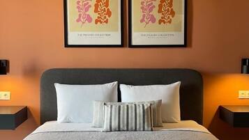A neatly made bed with white linens and two pillows, a dark headboard, and two framed artworks above the bed.