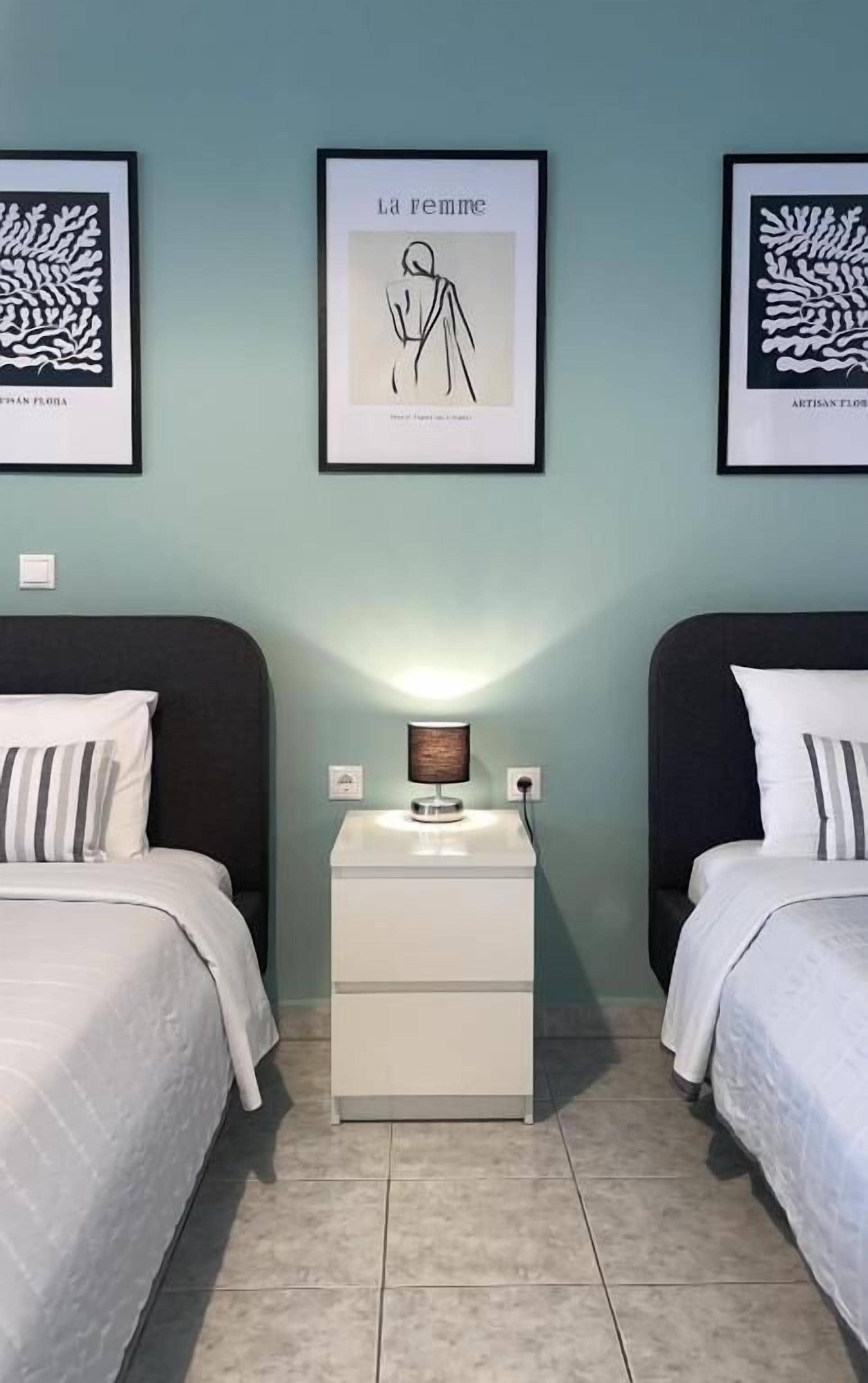 A hotel room with two beds, a nightstand with a lamp, and framed artwork on the wall.