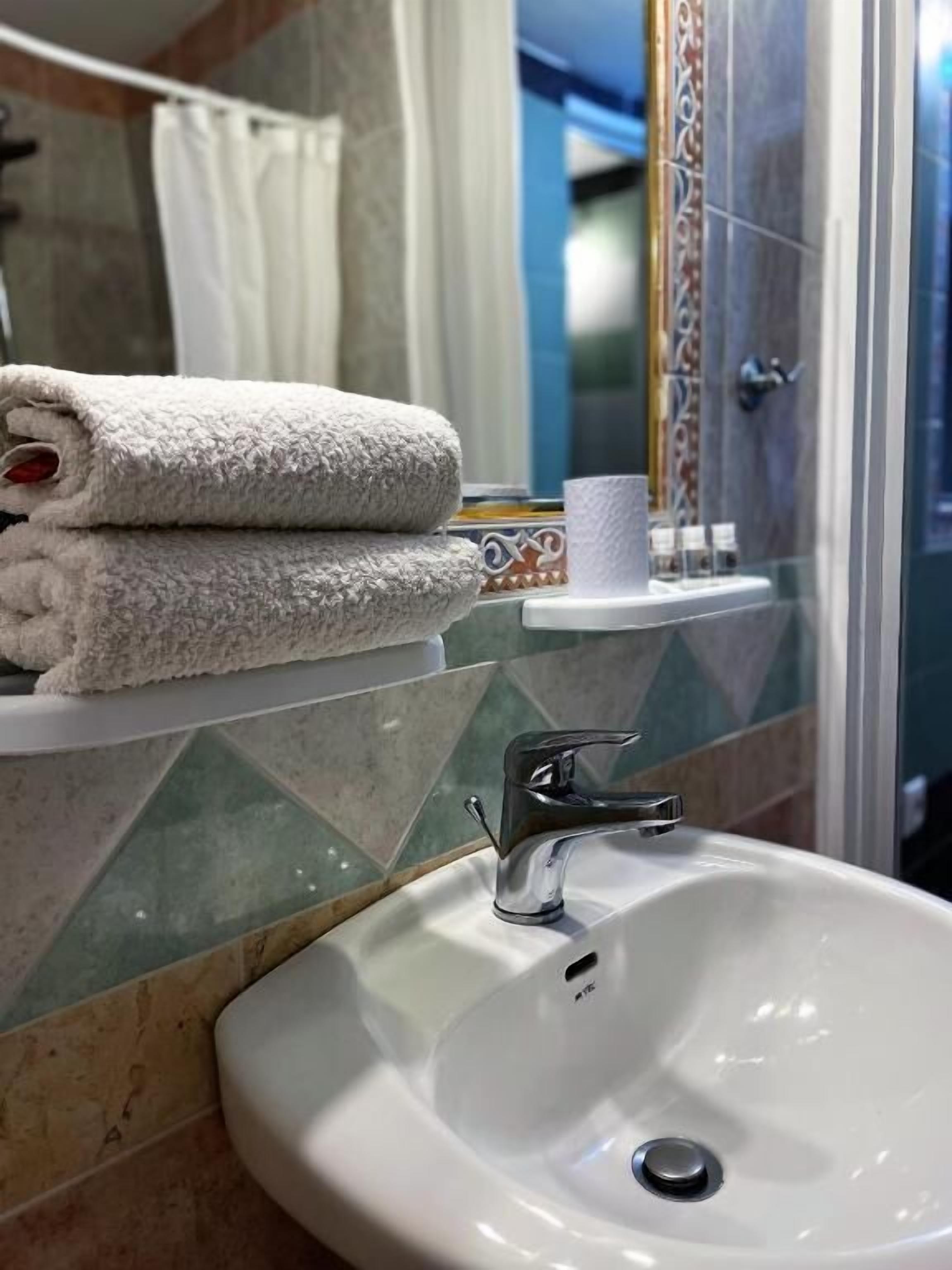 Un baño con un lavamanos blanco, un perchero con toallas dobladas y una zona de ducha.