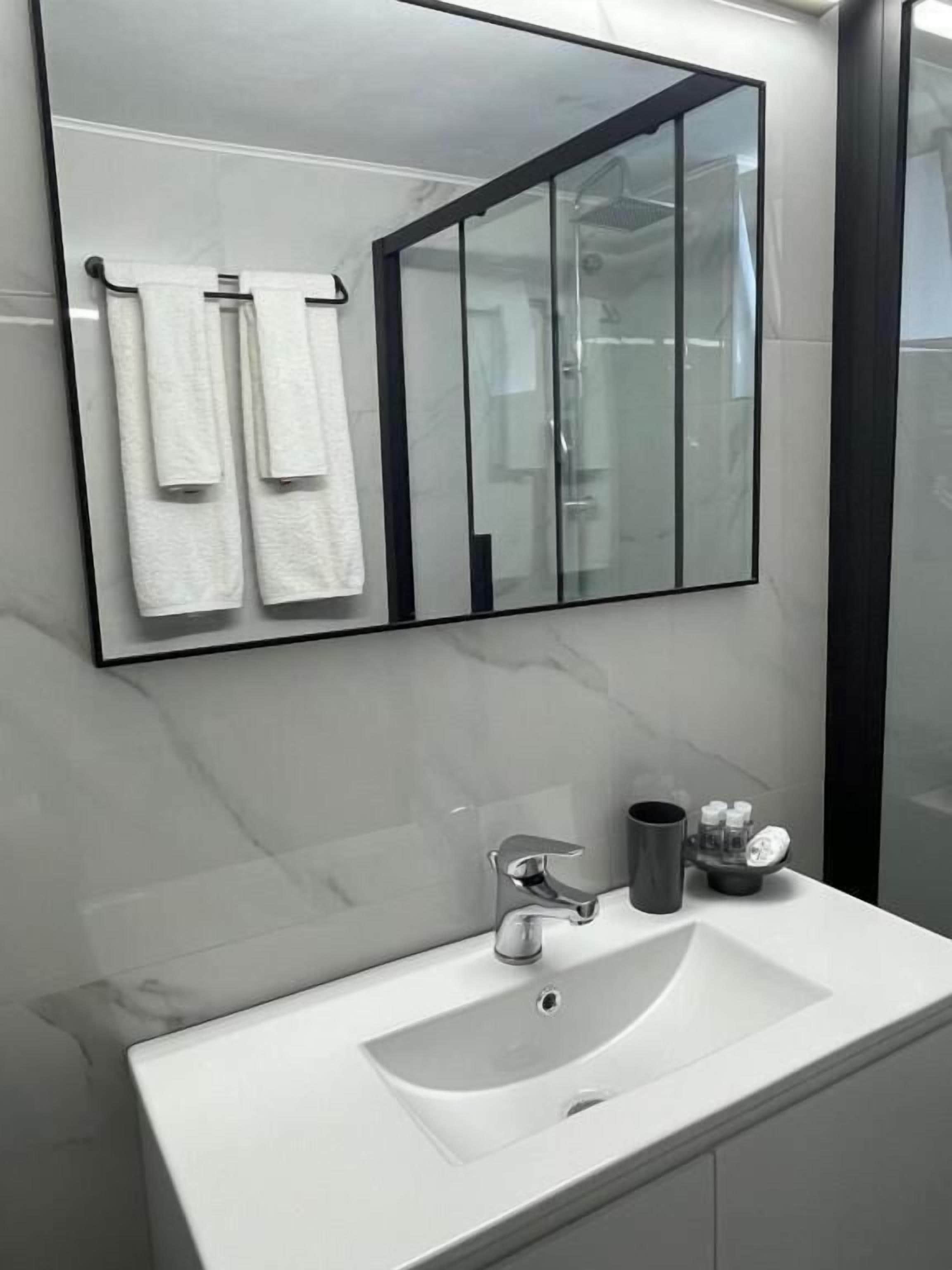 A modern bathroom with a large mirror, white sink, and a glass shower enclosure.