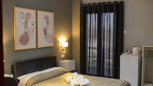 Une chambre d’hôtel comprenant un lit, une table de chevet, une lampe fixée au mur, un réfrigérateur et une fenêtre avec des rideaux.