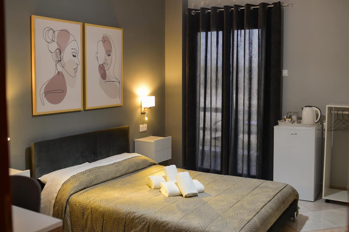 Ein Hotelzimmer mit einem Bett, einem Nachttisch, einer Wandlampe, einem Kühlschrank und einem Fenster mit Vorhängen.