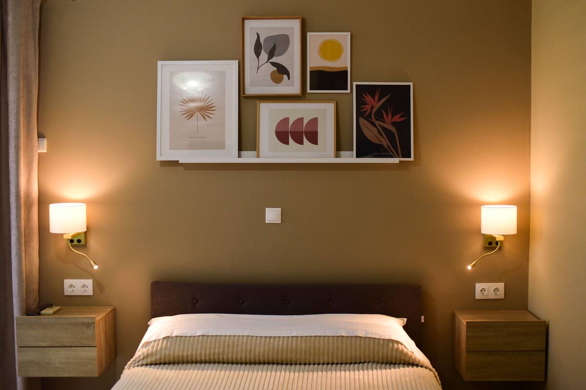 Ein Hotelzimmer mit einem Bett, Nachttischen, Wandlampen und gerahmten Kunstwerken.
