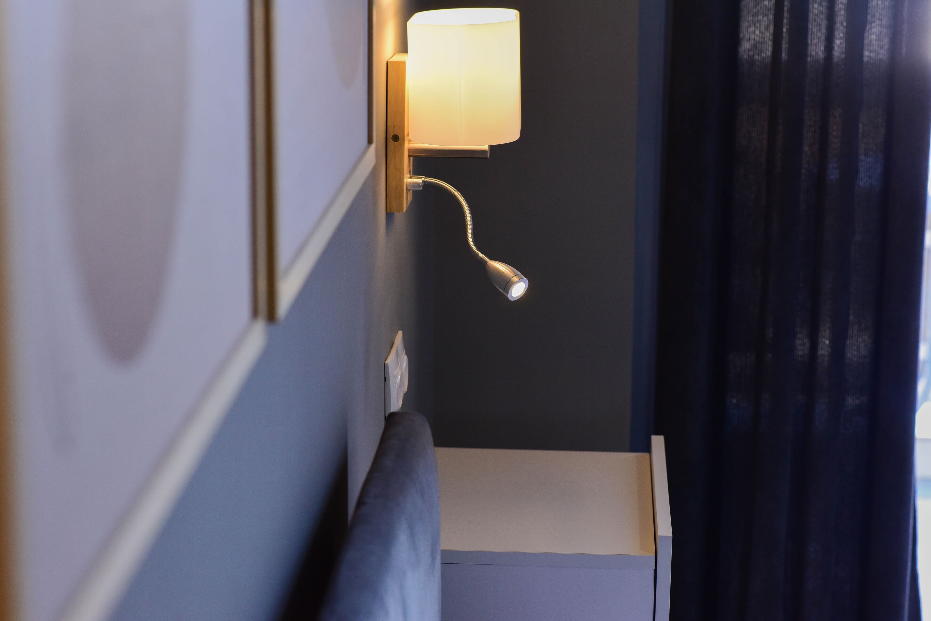 A corner of a room with a wall-mounted lamp, a dark curtain, and a piece of furniture against the wall.
