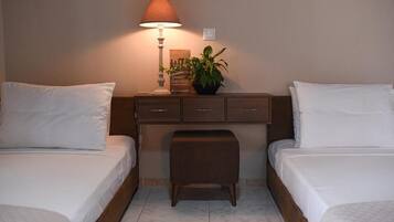 A hotel room with two beds, a nightstand, a lamp, a plant, and a small table.