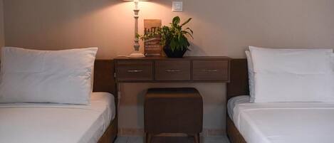 A hotel room with two beds, a nightstand, a lamp, a plant, and a small table.