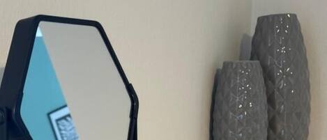 Una habitación moderna y minimalista con un estante blanco, un espejo geométrico y jarrones decorativos.