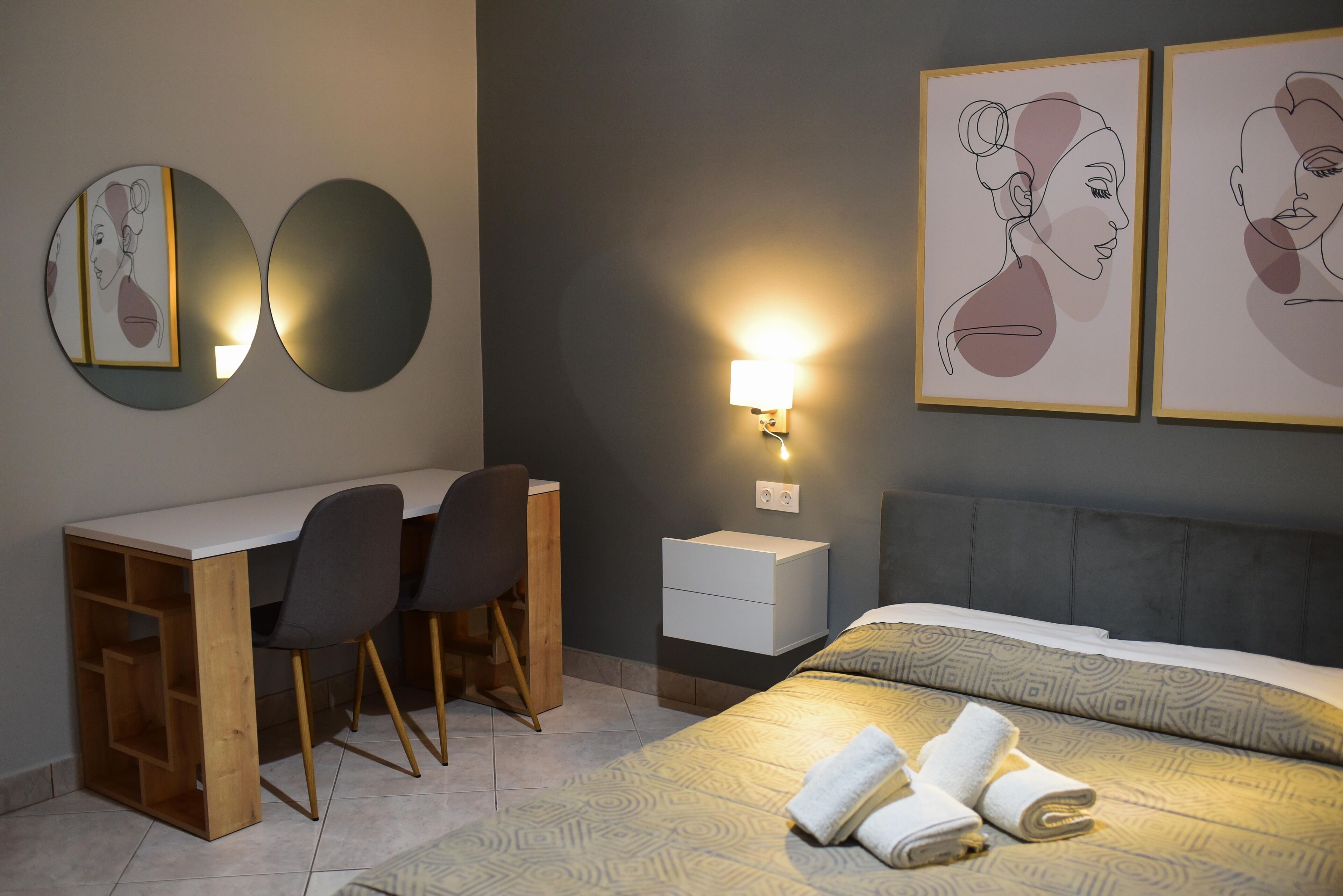 Una camera da letto moderna con una scrivania, due sedie, un comodino e un letto con copripiumino decorato.