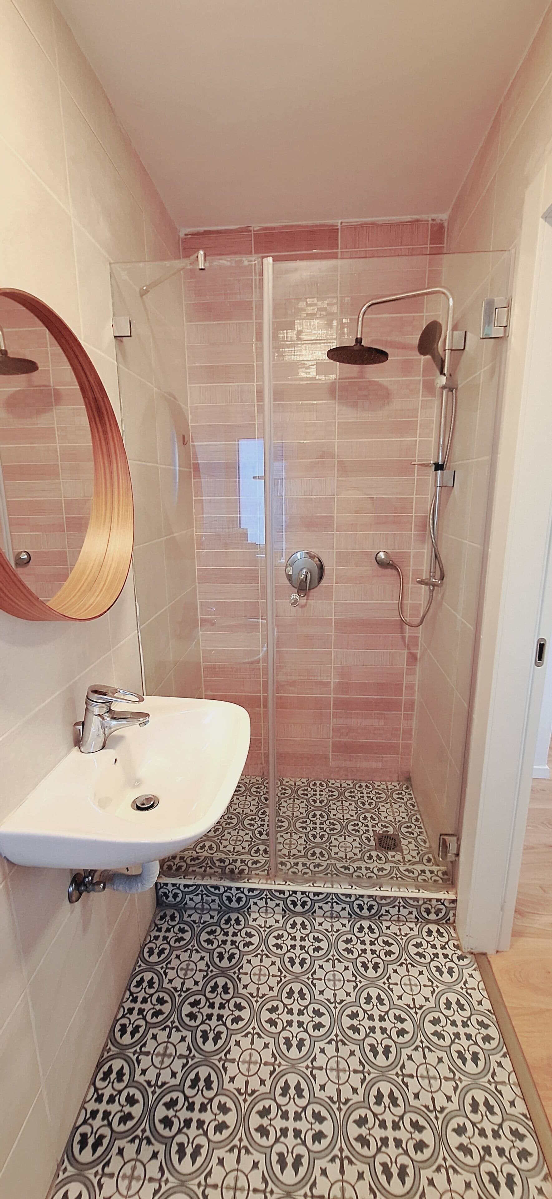 A bathroom with a glass-enclosed shower, a sink with a mirror, and patterned floor tiles.