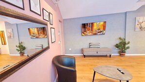 A modern living room with a sofa, a round coffee table, and a black chair. There are framed artworks on the walls and a large window with a view. - JAKO Boutique (Jerusalem)