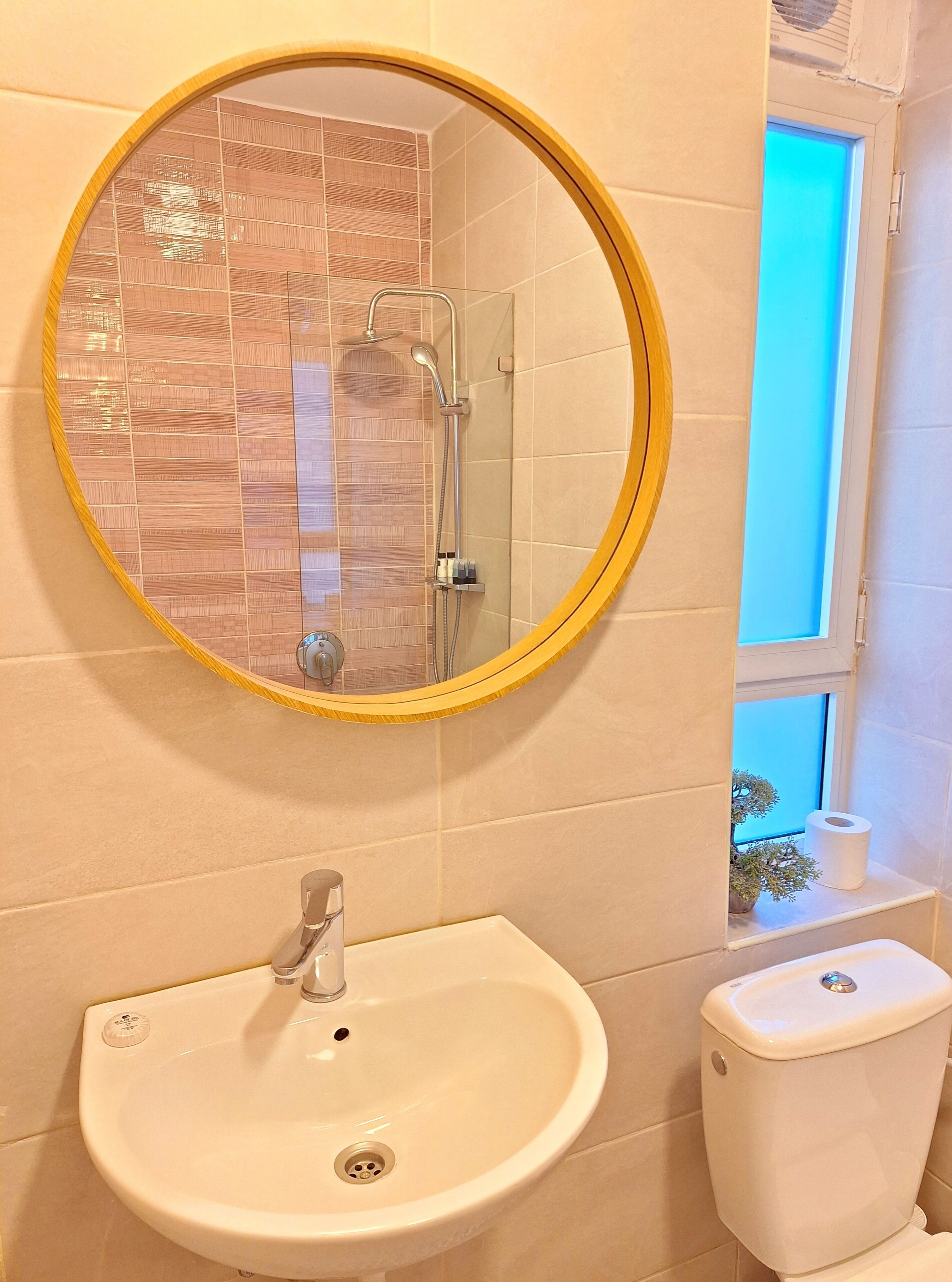 Un baño con un espejo redondo, un lavamanos y un inodoro.