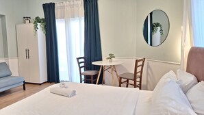 A hotel room with a bed, a desk, two chairs, a wardrobe, a mirror, and a potted plant. - JAKO Boutique (Jerusalem)