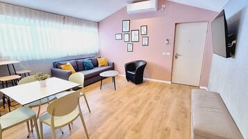 A modern living room with a sofa, dining table, chairs, and a TV mounted on the wall.
