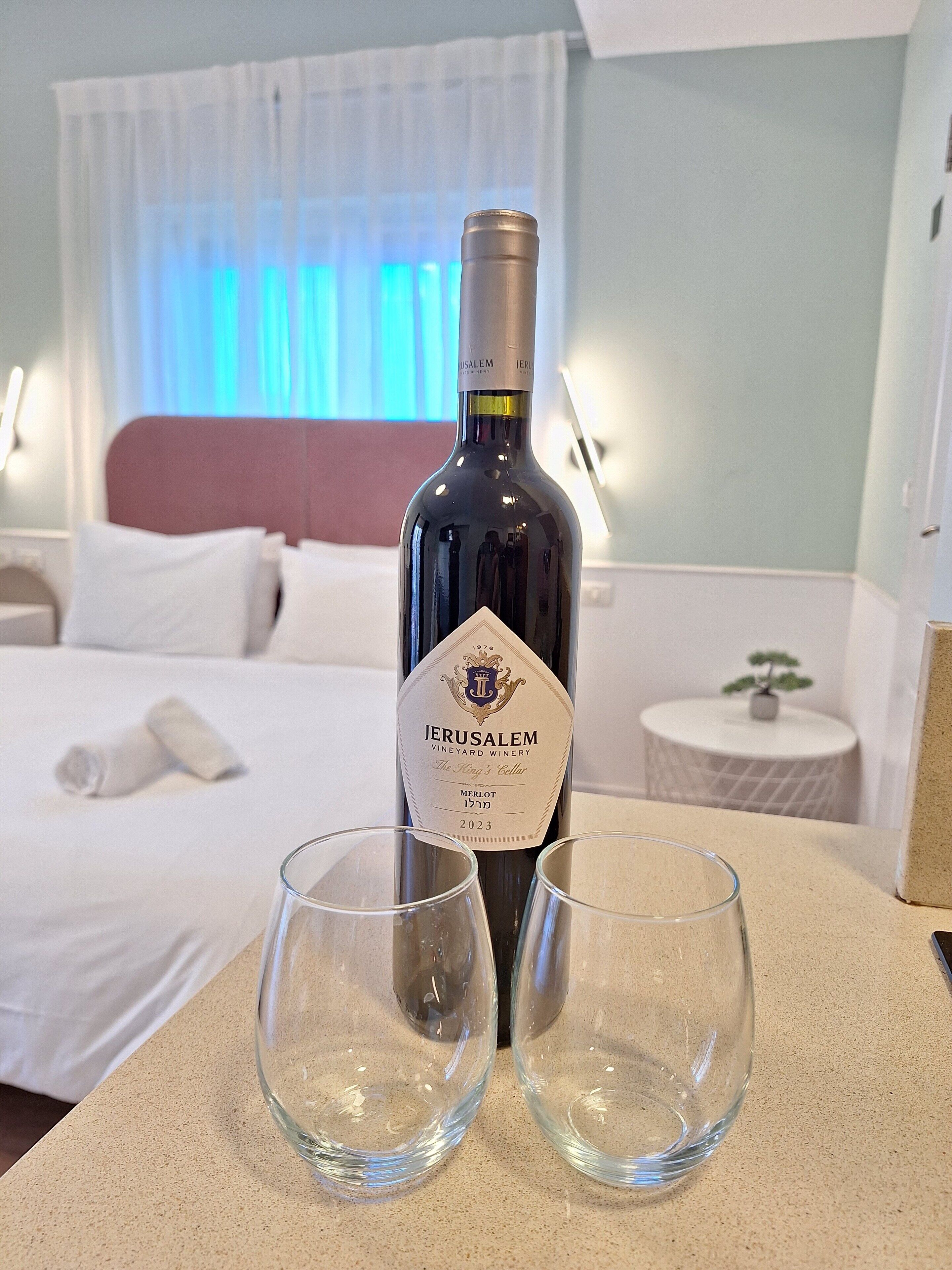 Una botella de Merlot de la bodega Viñedos de Jerusalén, número 17, sobre una mesa con dos copas vacías.