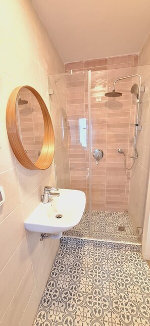 Een badkamer met een douche, wastafel en spiegel.