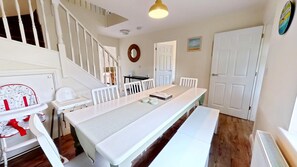 A dining area with a long table, white chairs, a high chair, and a staircase.