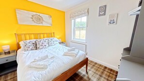 A bedroom with a bed, a nightstand, a lamp, a window with curtains, and a radiator.