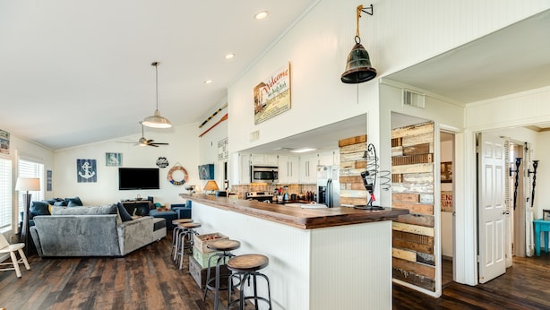 A spacious living area with a large sofa, a kitchen with wooden accents, and a bar area with stools.