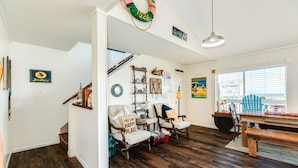A spacious living room with a wooden floor, two armchairs, a dining table, and a large window.