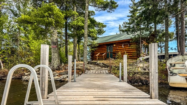 A wooden dock leading to a log cabin with a metal railing and a boat docked nearby. - Beautiful Private Island Getaway-Boat Rental Available! (Tower)