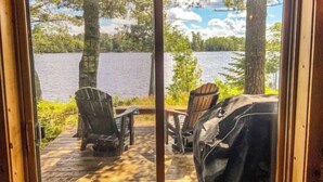A wooden deck with two Adirondack chairs and a grill, overlooking a lake with trees and a cloudy sky. - Beautiful Private Island Getaway-Boat Rental Available! (Tower)