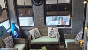 Ein gemütliches Zimmer mit Korbmöbeln, einer Couch mit marineblauen Kissen, einem aufgehängten Hut und einer kleinen Pflanze auf einem Tisch.