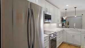Una cocina moderna con electrodomésticos de acero inoxidable, armarios blancos e iluminación colgante.