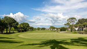 Un campo de golf con un estanque, árboles y casas al fondo.