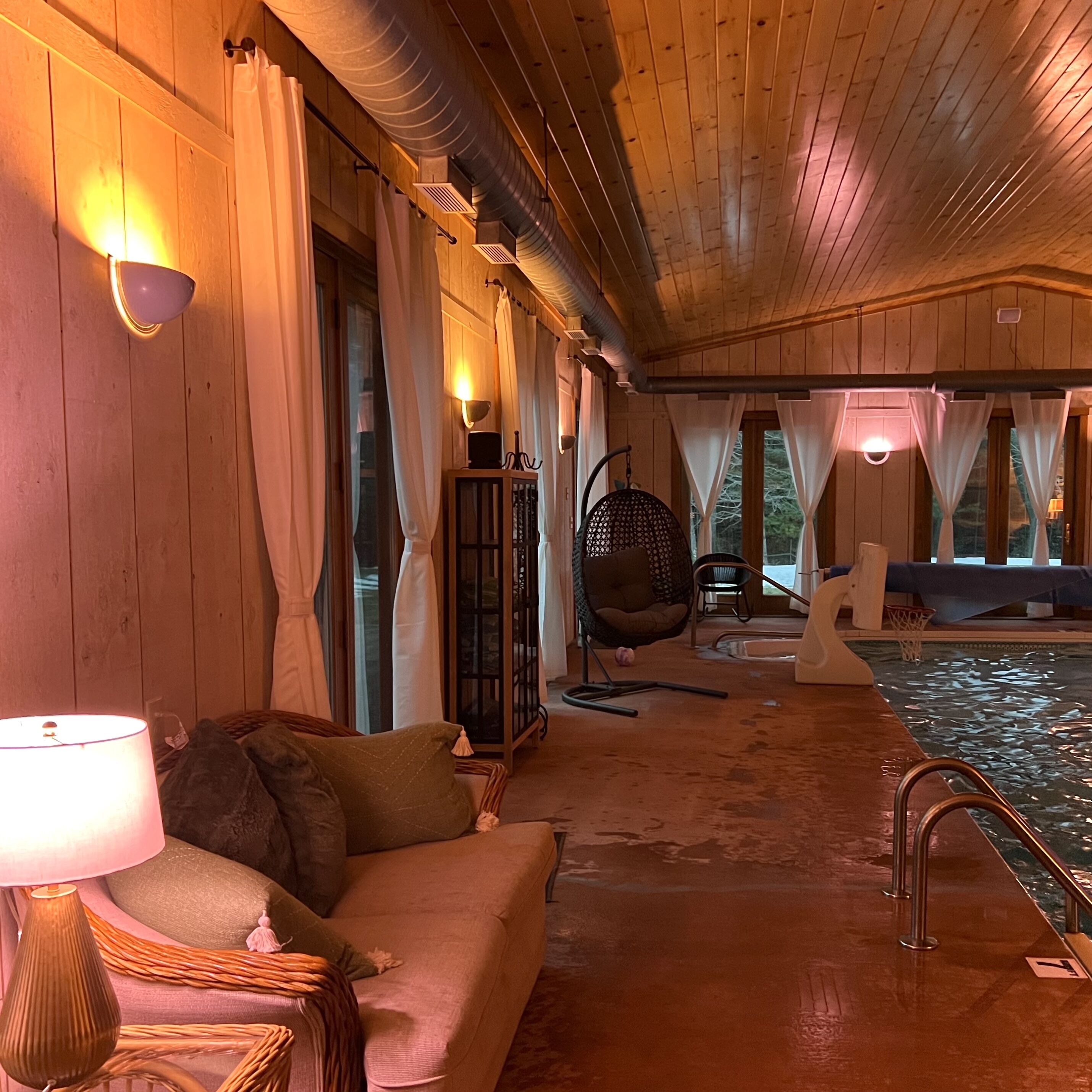 Un intérieur en bois avec un canapé, un fauteuil suspendu et un espace piscine.
