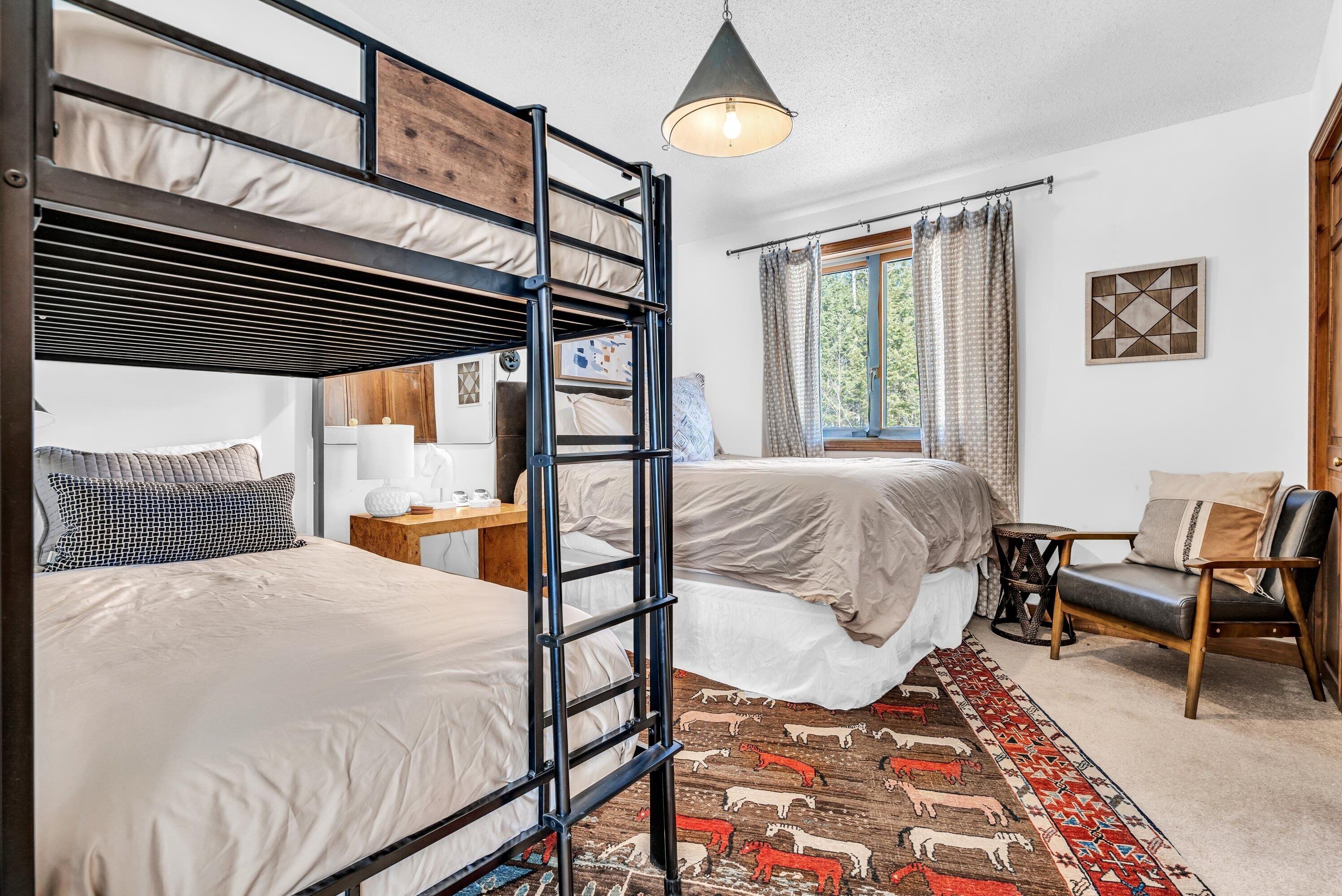 A room with bunk beds, a desk, a chair, a rug, and a window with curtains.