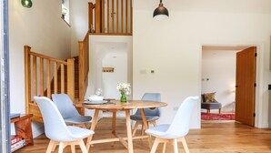 A dining area with a wooden table and four chairs, a staircase, and a hanging light fixture. - Bluebell Cottage (Tavistock)