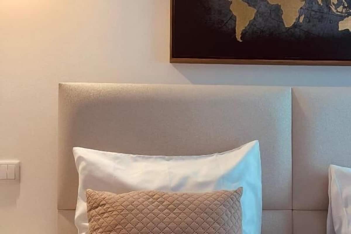 Una cama bien hecha con dos almohadas, un mapa mundial en la pared y una mesita de noche con una lámpara.