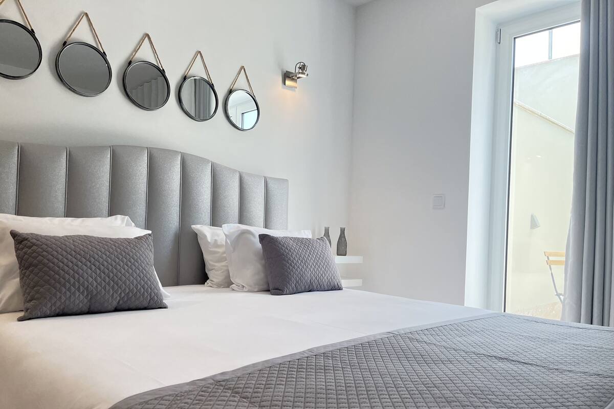Un dormitorio moderno con una cama grande, cabecera gris y varios espejos colgados en la pared.