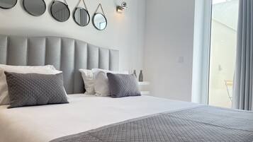 A modern bedroom with a large bed, grey headboard, and multiple wall-mounted mirrors.