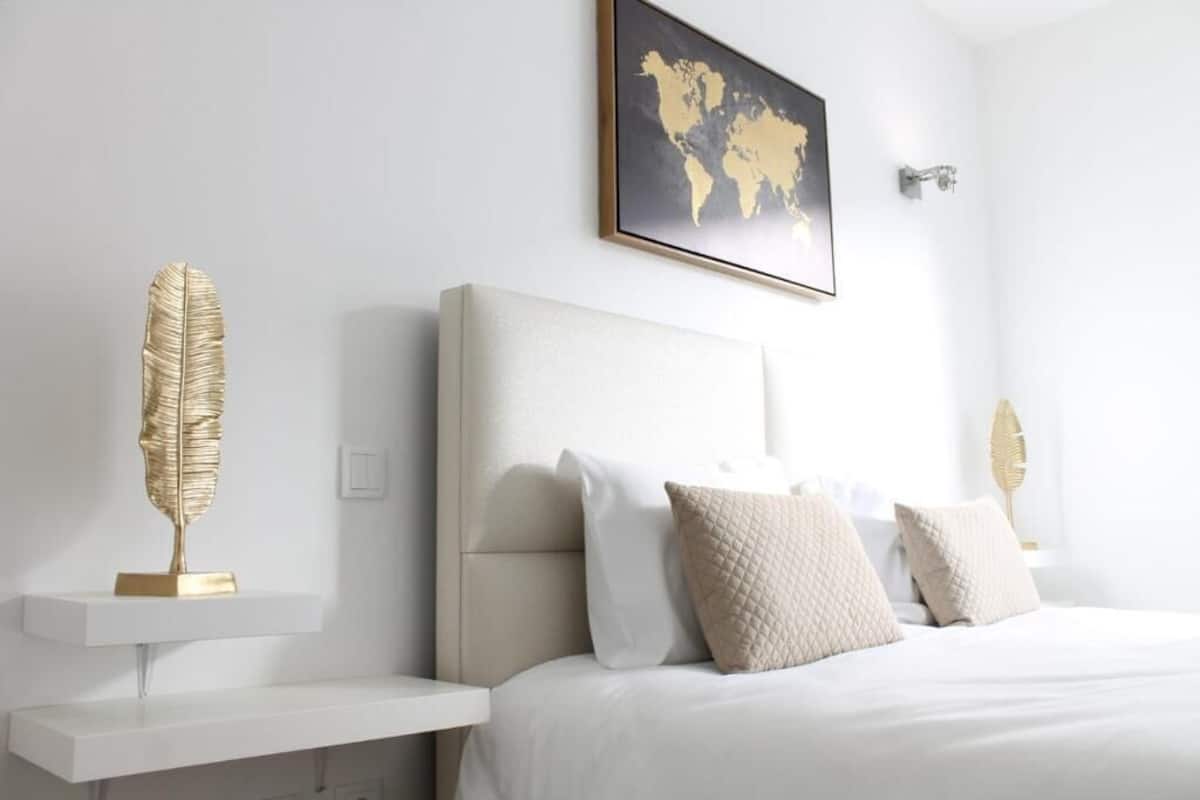 Un dormitorio moderno con una cama grande, cabecera blanca y hojas doradas decorativas en estantes.