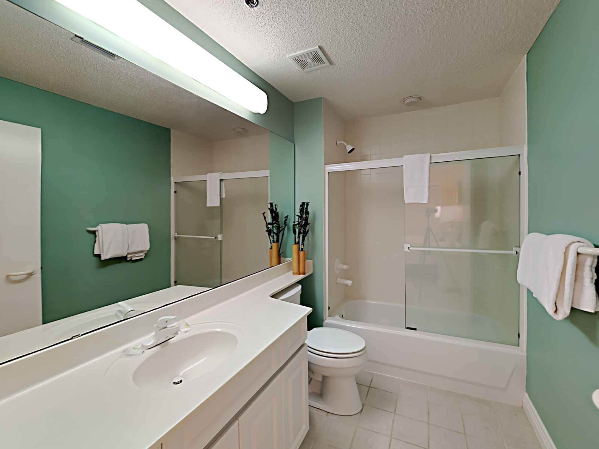 A modern bathroom with a large mirror, white sink, toilet, and glass-enclosed shower.