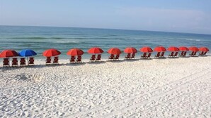 A beach with rows of red and blue beach umbrellas and chairs.