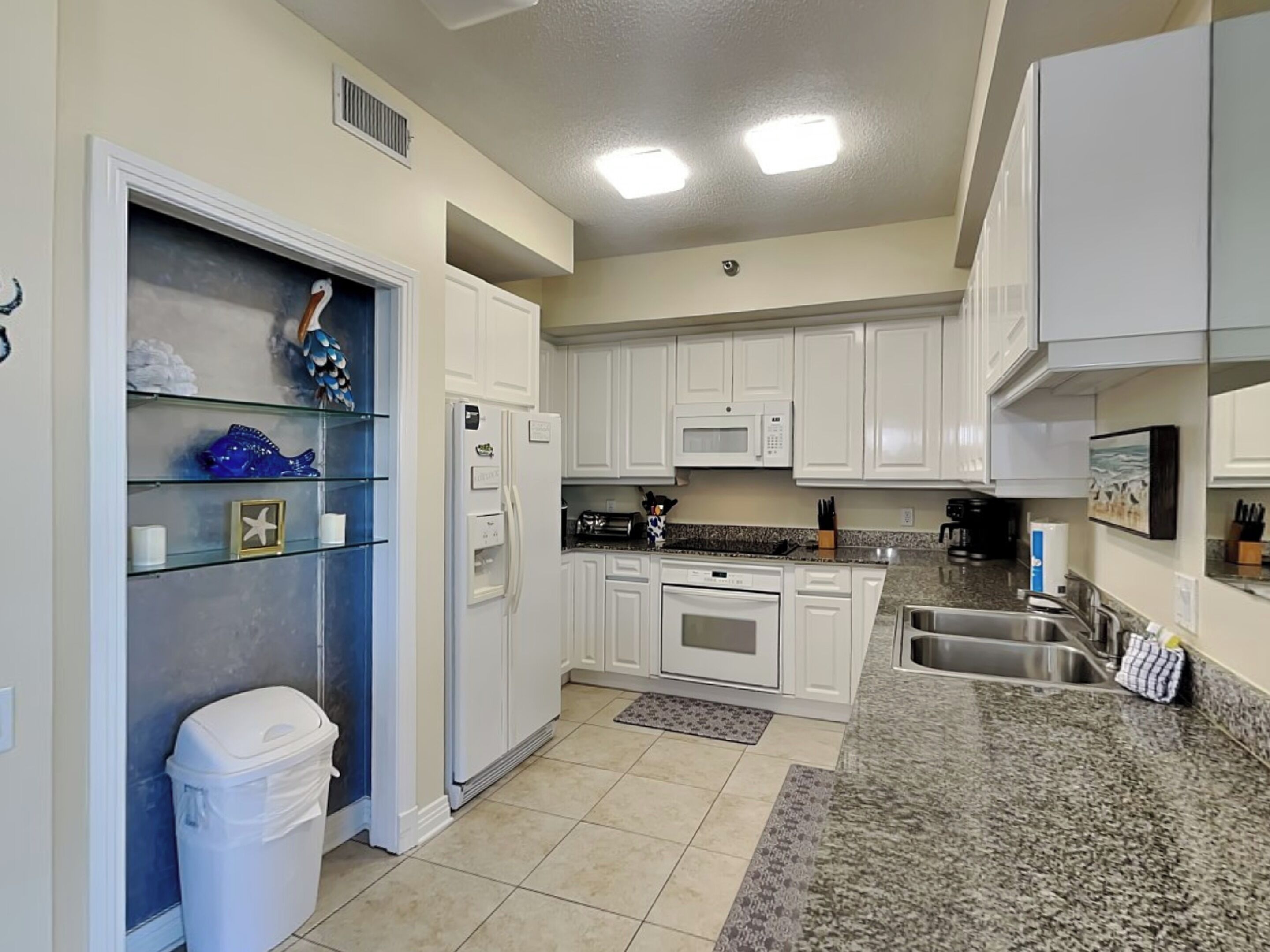 A kitchen with white cabinets, a microwave, a refrigerator, a sink, and a trash bin.