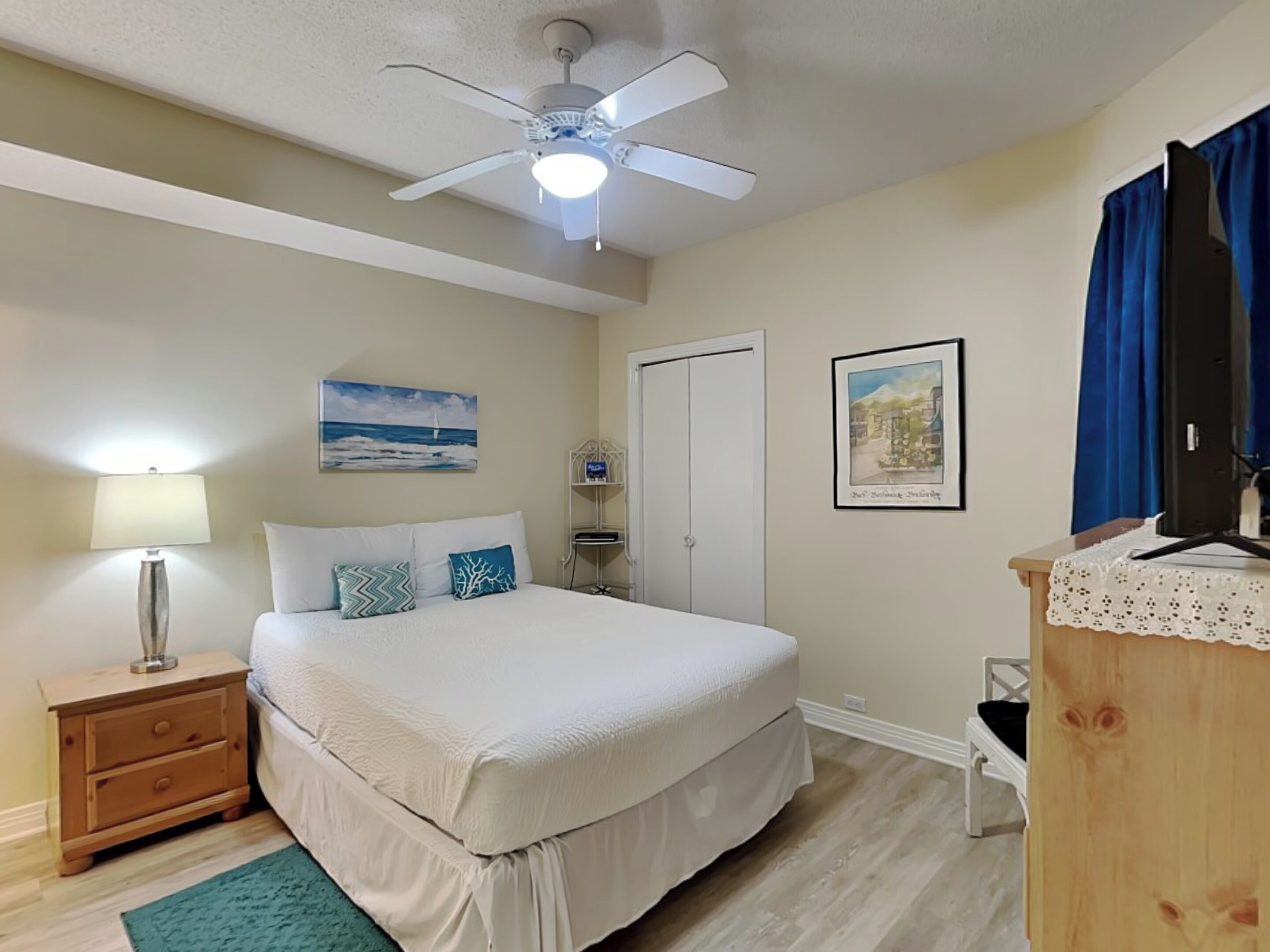 A bedroom with a bed, a nightstand, a lamp, a ceiling fan, a door, and a dresser.