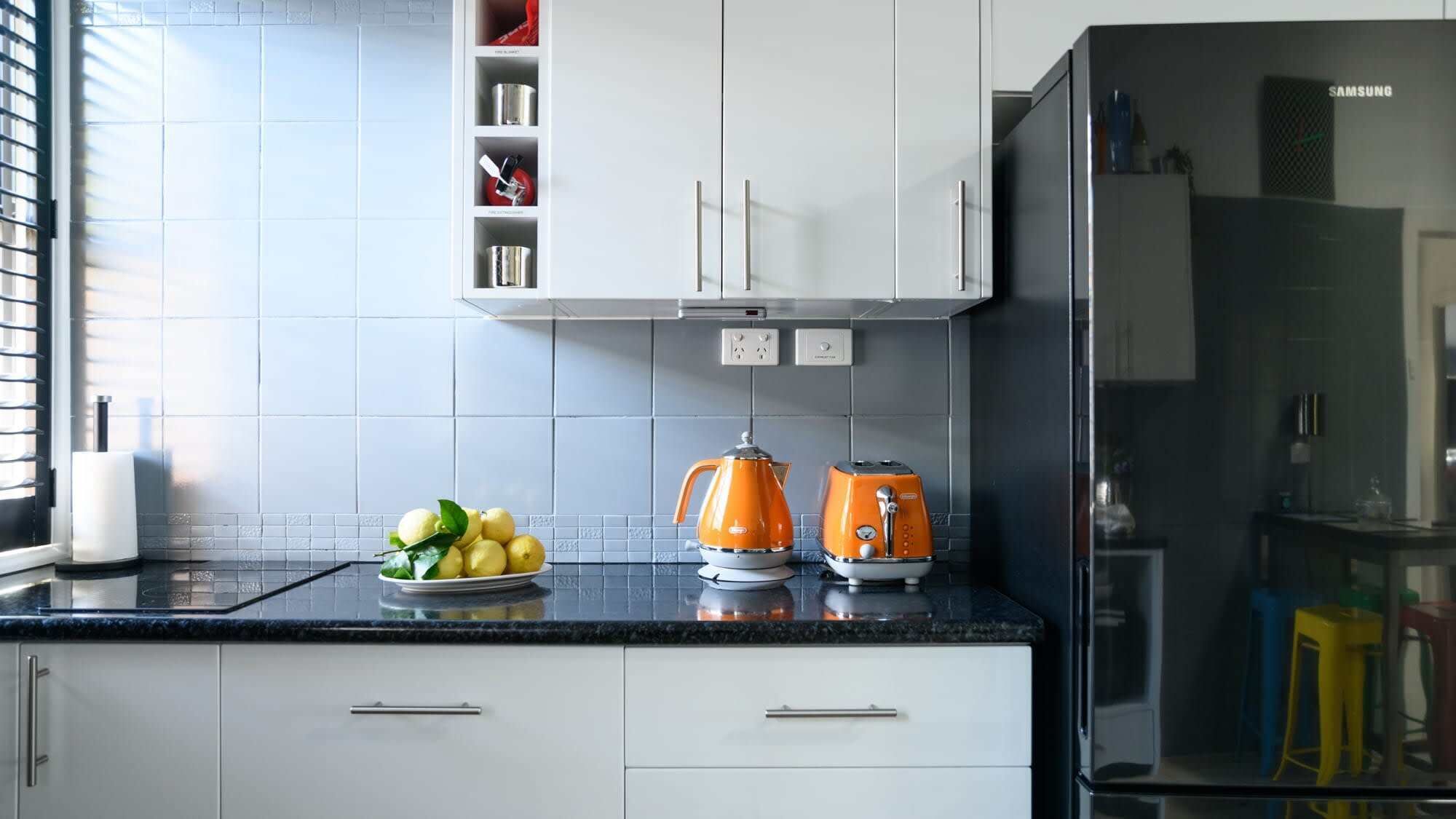 A kitchen with white cabinets, a black refrigerator, and two orange kettles on the counter.