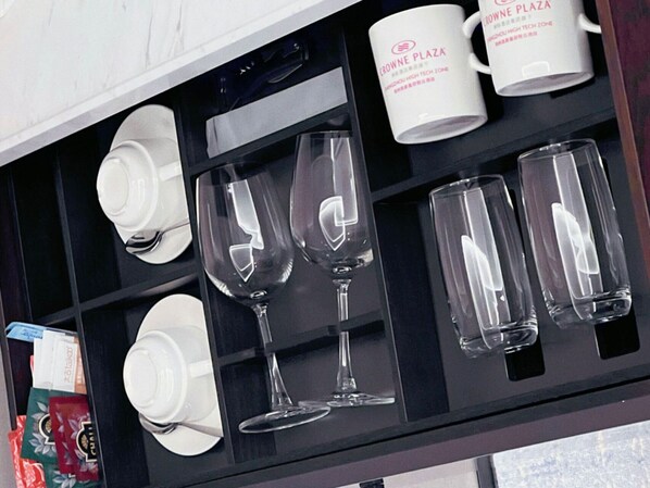 A storage unit with white mugs and clear glassware.