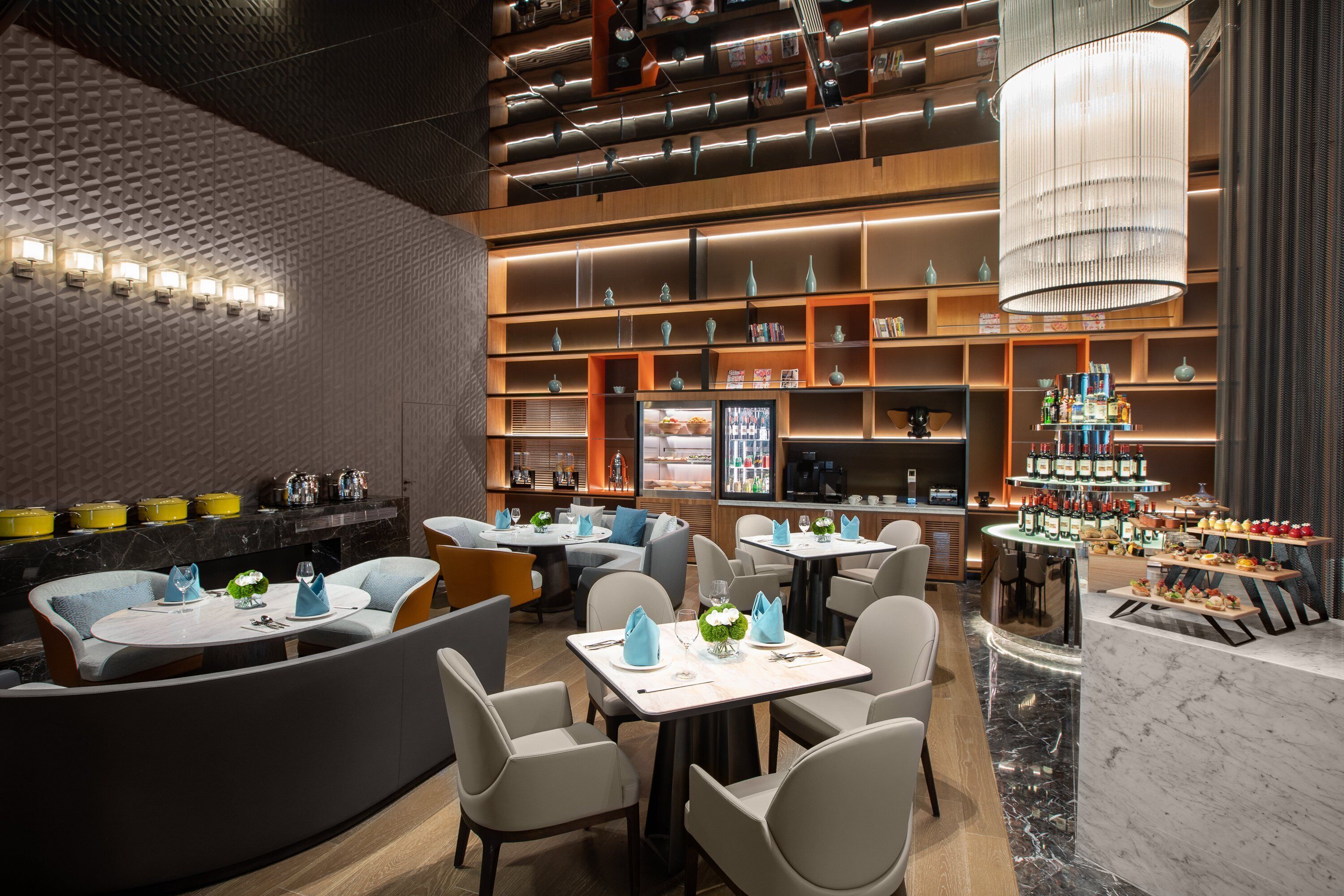 A modern restaurant with multiple seating areas, including round tables and booths, and a bar area with a variety of bottles.
