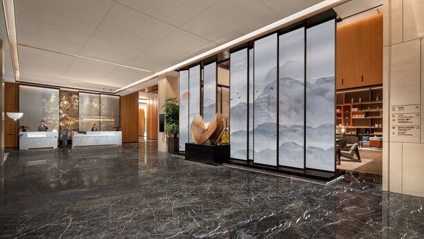 Een moderne lobby met een marmeren vloer, receptiebalie en een groot abstracte sculptuur.