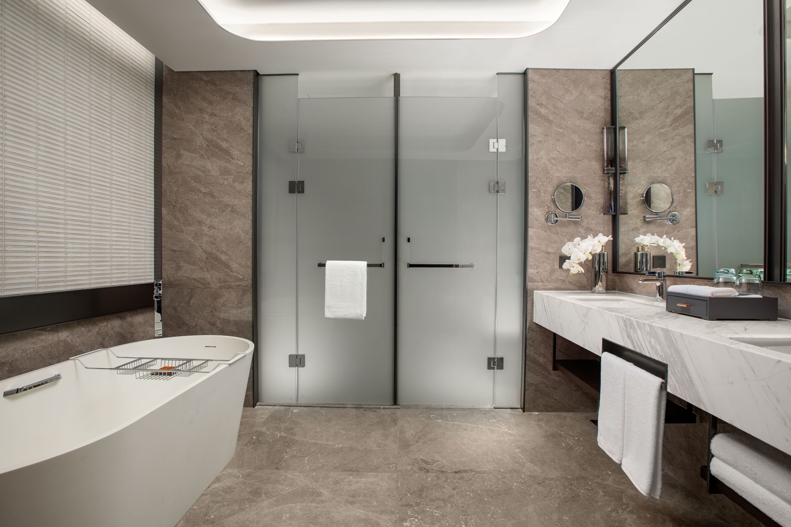 A modern bathroom with a curved bathtub, a large mirror, and a vanity with a marble countertop.