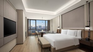Een moderne hotelkamer met een groot bed, een flatscreen televisie, een bureau met een stoel en uitzicht op de stad.