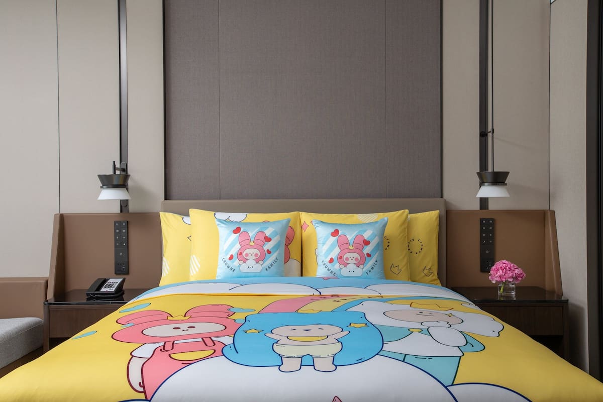 Een hotelkamer met een bed, twee nachtkastjes, een lamp en een bloevas.