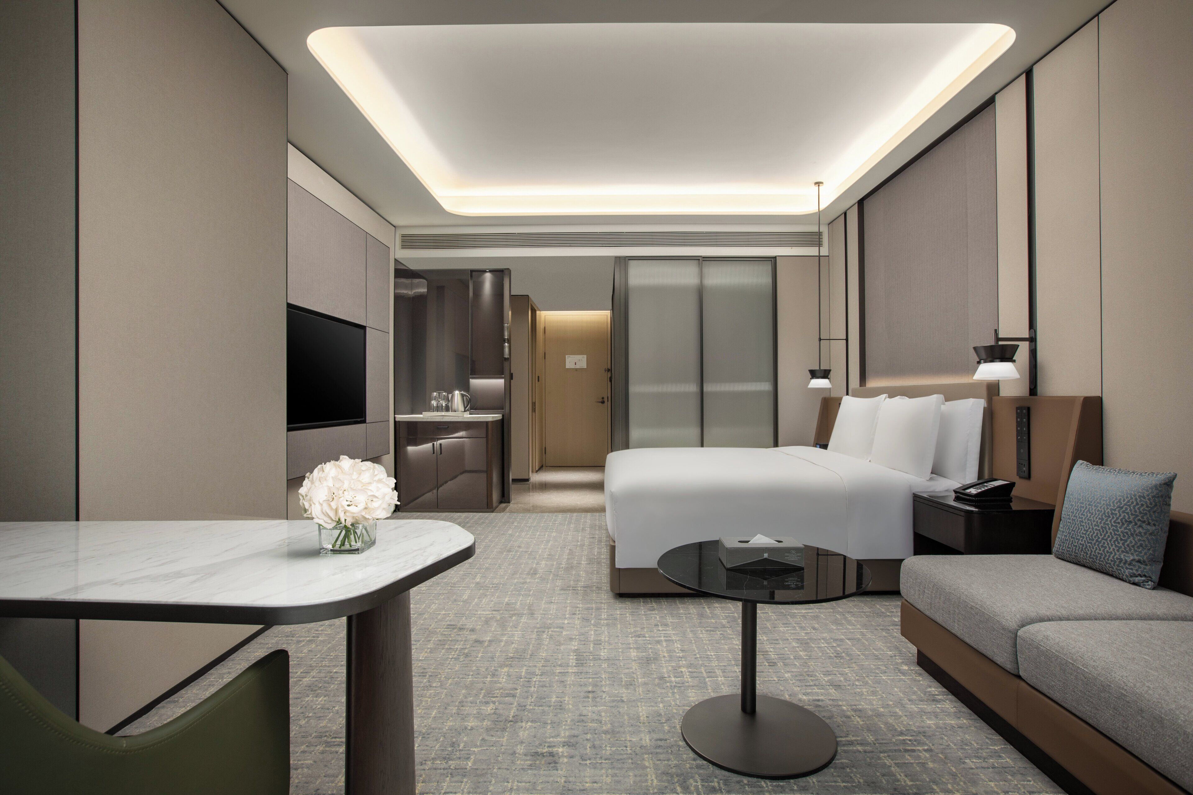 Quarto de hotel moderno com cama, sofá, escrivaninha e televisão.