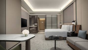 Quarto de hotel moderno com cama, sofá, escrivaninha e televisão.